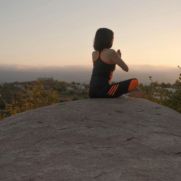 Person meditating peacefully outdoors during a sunset.
